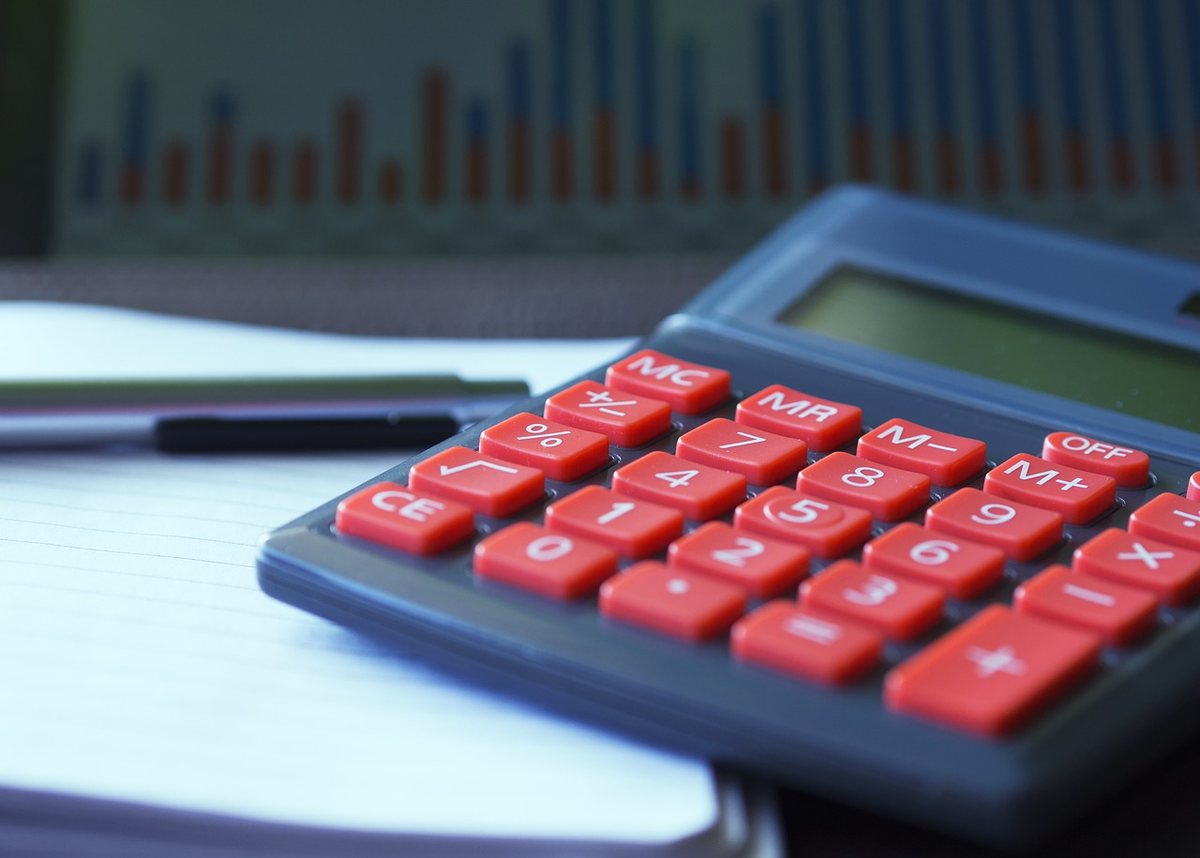 Calculatrice avec boutons rouges sur une feuille blanche, stylo et graphique flou en arrière-plan