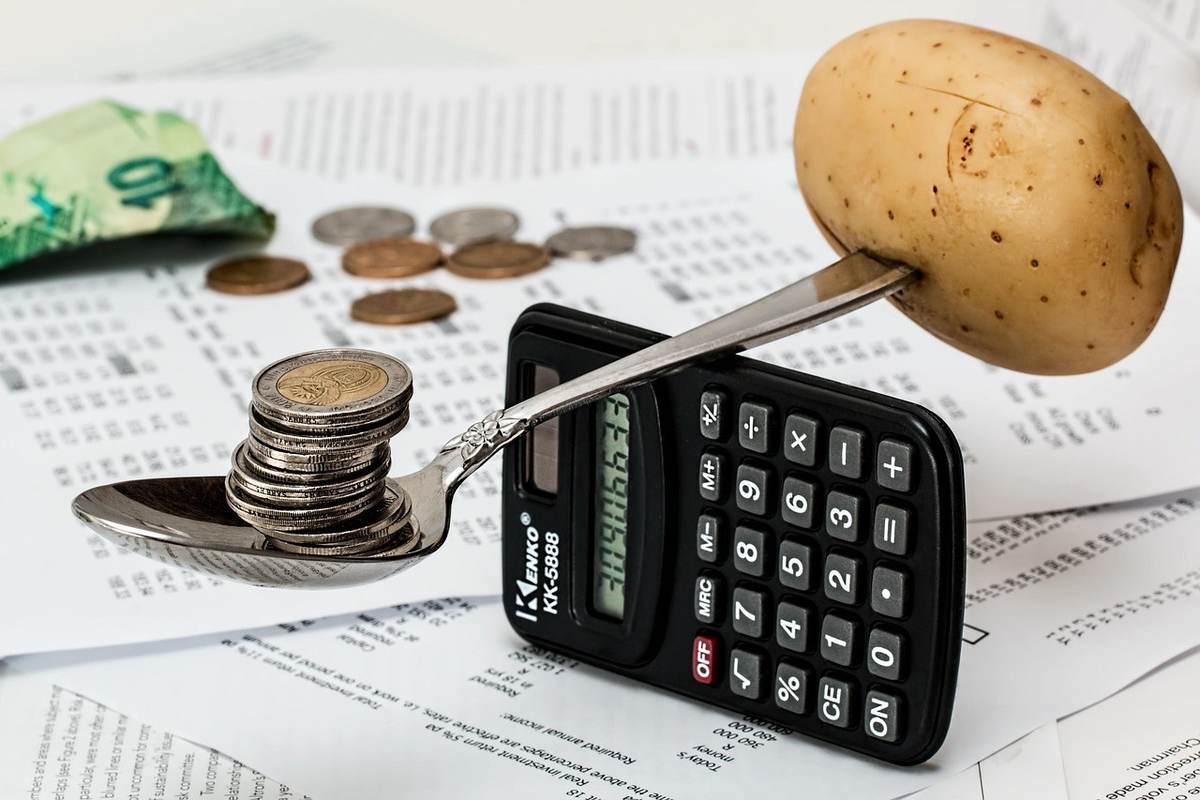 Une cuillère avec des pièces et une pomme de terre sur une calculatrice Une cuillère avec des pièces et une pomme de terre sur une calculatrice