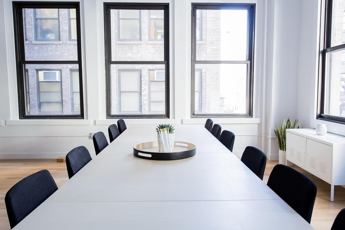 Longue table blanche, chaises noires, grandes fenêtres, vase central Longue table blanche, chaises noires, grandes fenêtres, vase central