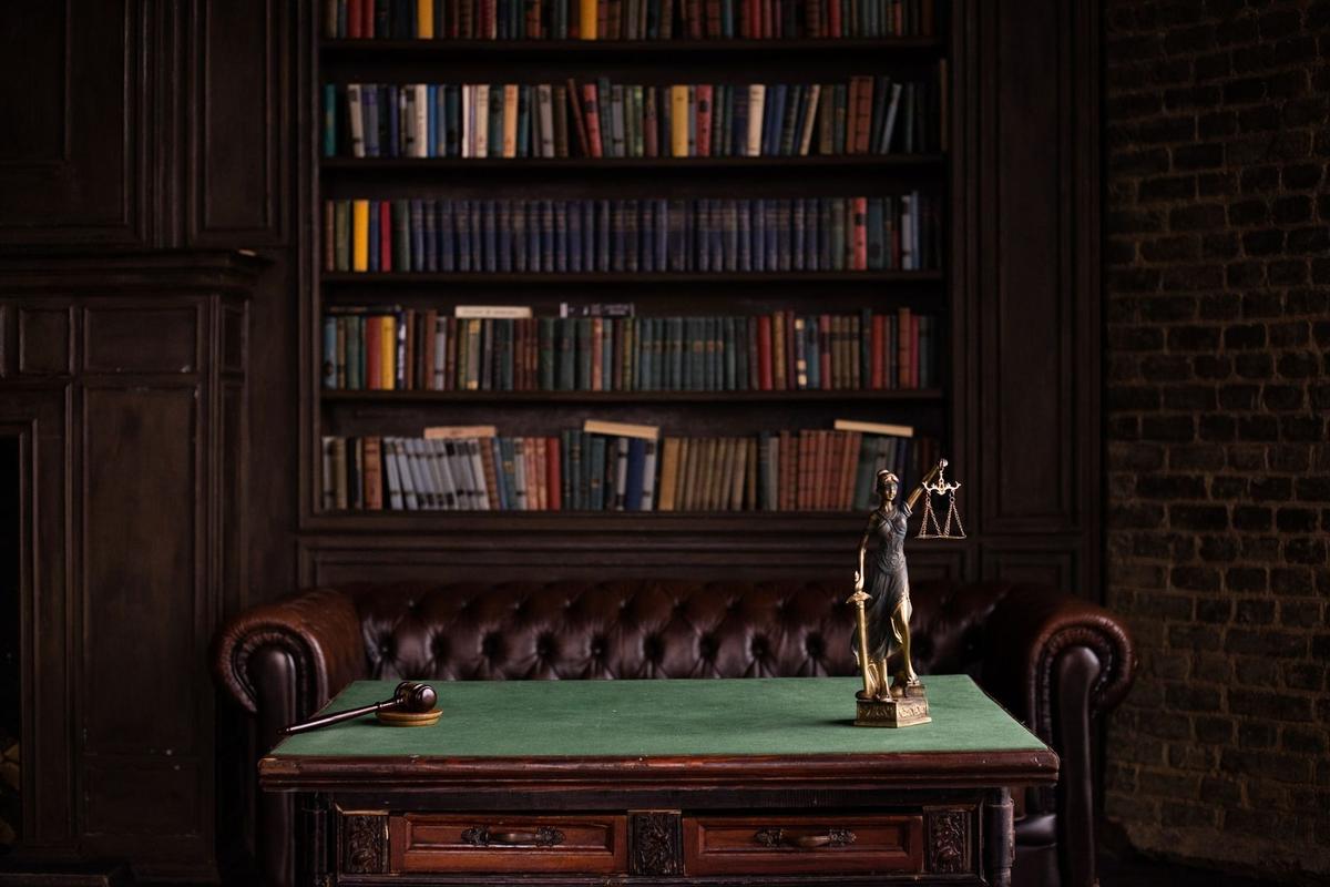 Étagère de livres, bureau avec tapis vert et statue de la justice dans un salon sombre Étagère de livres, bureau avec tapis vert et statue de la justice dans un salon sombre